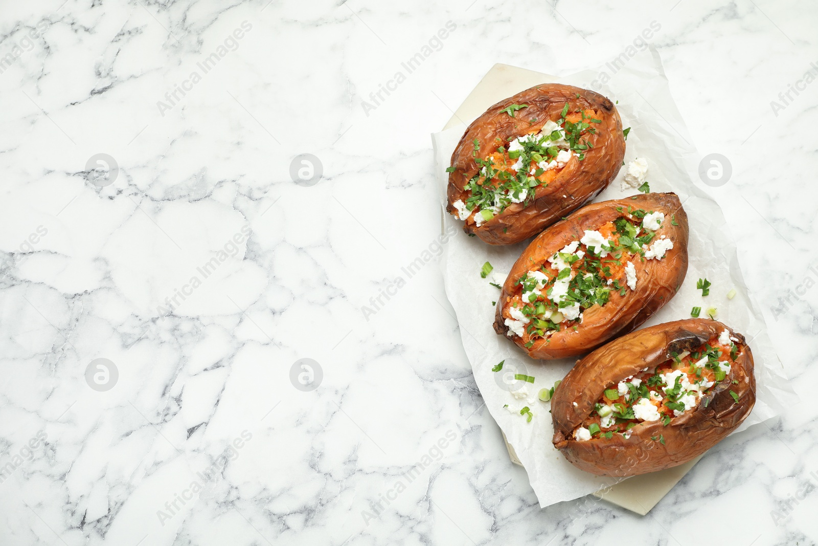 Photo of Tasty cooked sweet potatoes with feta cheese, green onion and parsley on white marble table, top view. Space for text