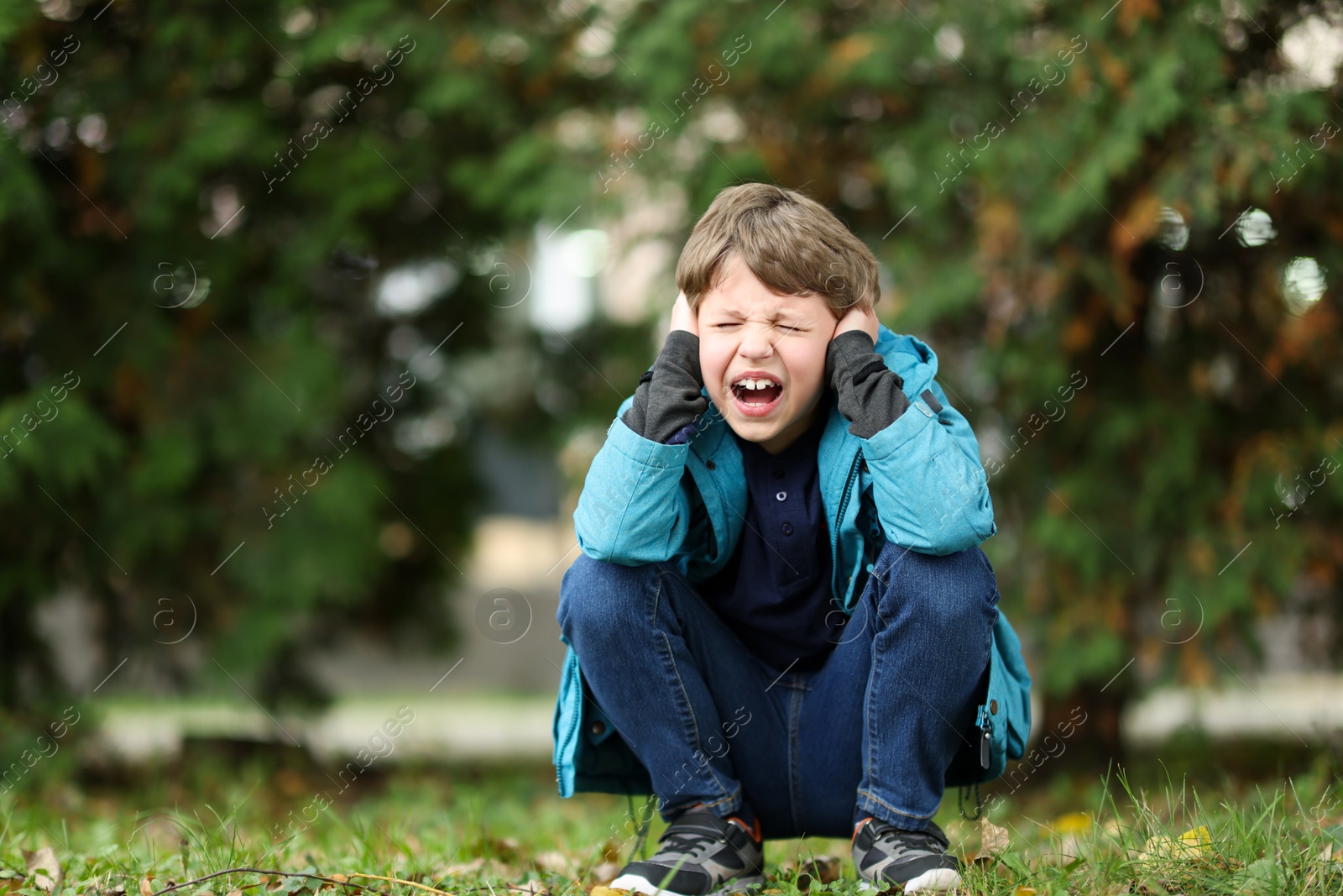 Photo of Autism concept. Scared little boy covering his ears outdoors, space for text