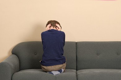 Photo of Autism concept. Lonely little boy covering his ears on sofa at home, back view