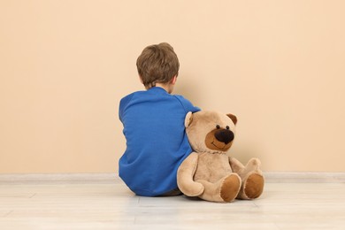 Photo of Autism concept. Lonely little boy with teddy bear on floor at home, back view