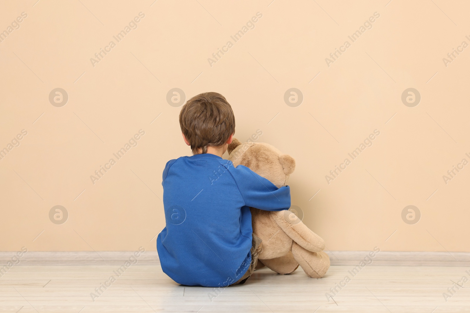 Photo of Autism concept. Lonely little boy with teddy bear on floor at home, back view