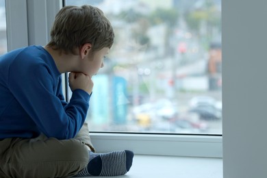 Photo of Autism concept. Lonely little boy near window at home, space for text