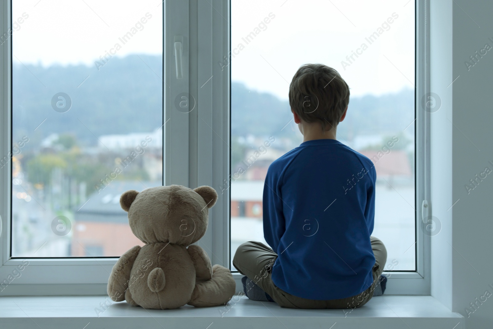 Photo of Autism concept. Lonely little boy with teddy bear near window at home, back view