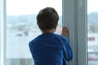 Autism concept. Lonely little boy near window at home, back view