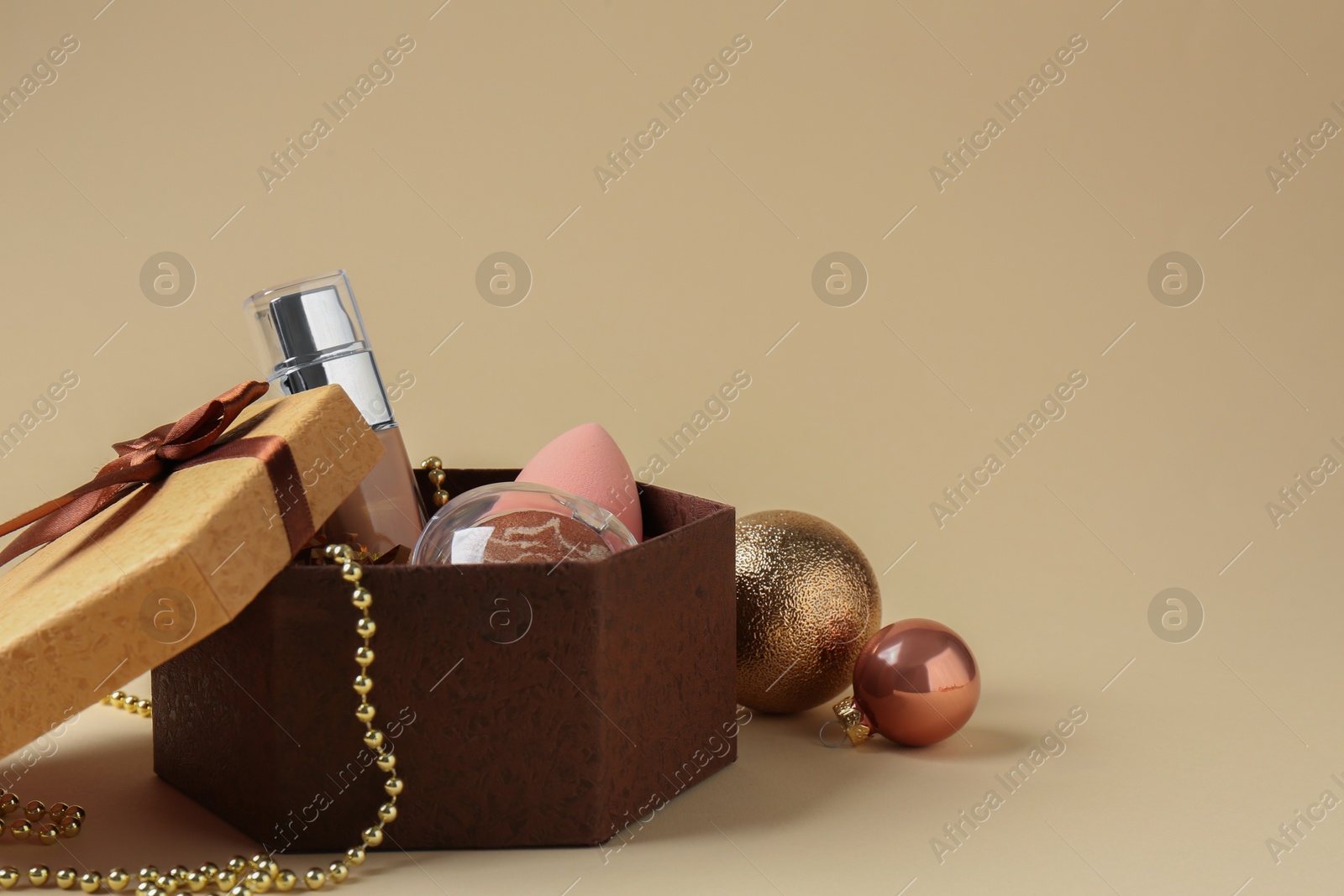 Photo of Cosmetic products in gift box and Christmas balls on beige background, space for text