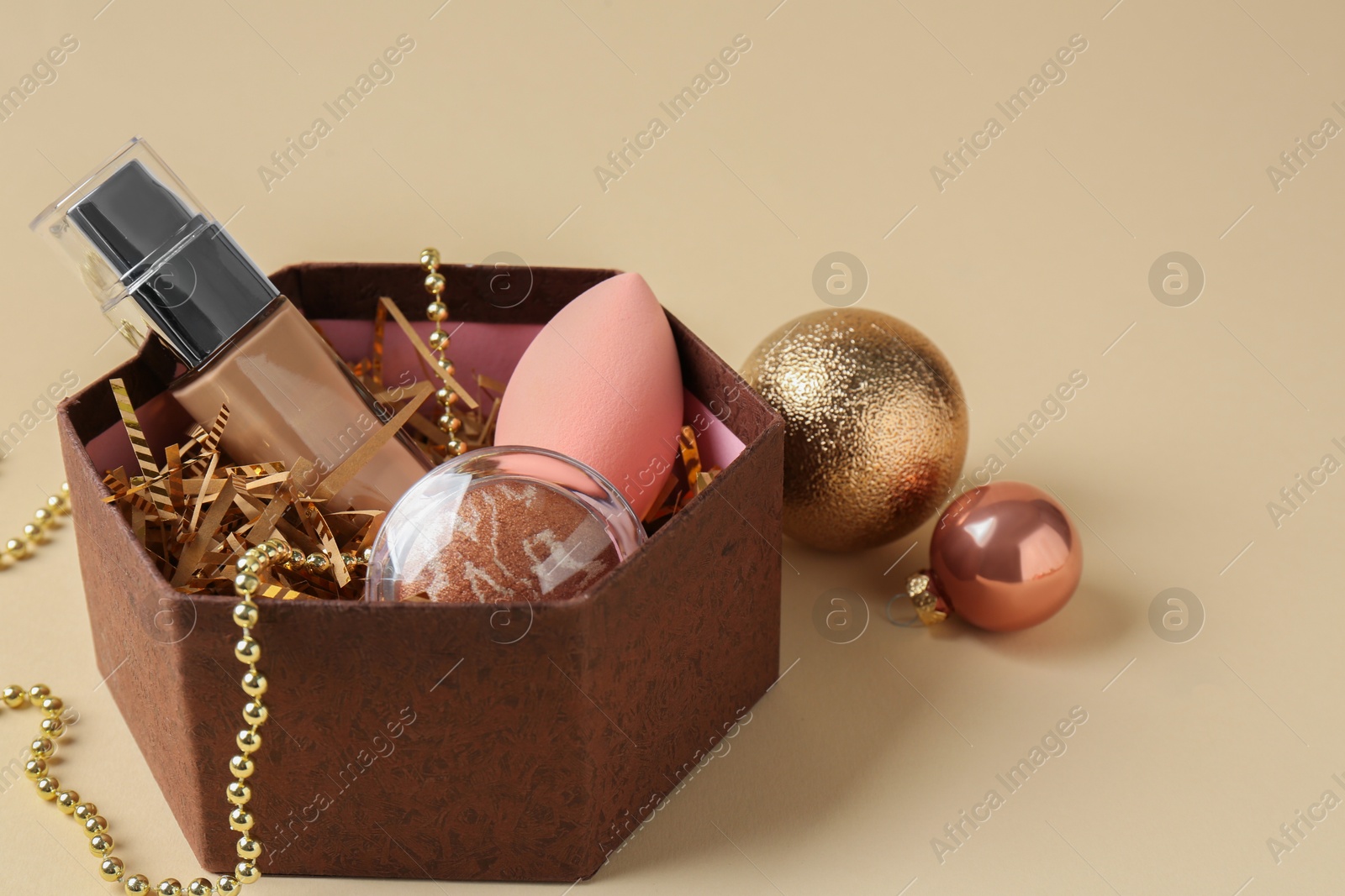 Photo of Cosmetic products in gift box and Christmas balls on beige background, space for text