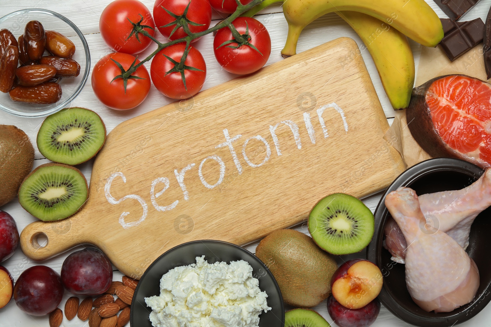 Photo of Wooden board with word Serotonin and different fresh products on white table, flat lay