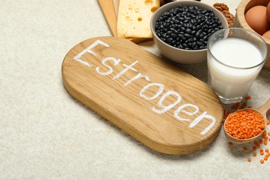 Photo of Wooden board with word Estrogen and different fresh products on light textured table