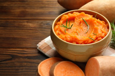 Photo of Tasty mashed sweet potato with rosemary in bowl and fresh vegetables on wooden table, closeup. Space for text