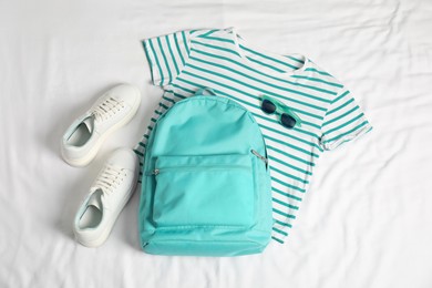 Photo of Stylish outfit with backpack on white fabric, flat lay