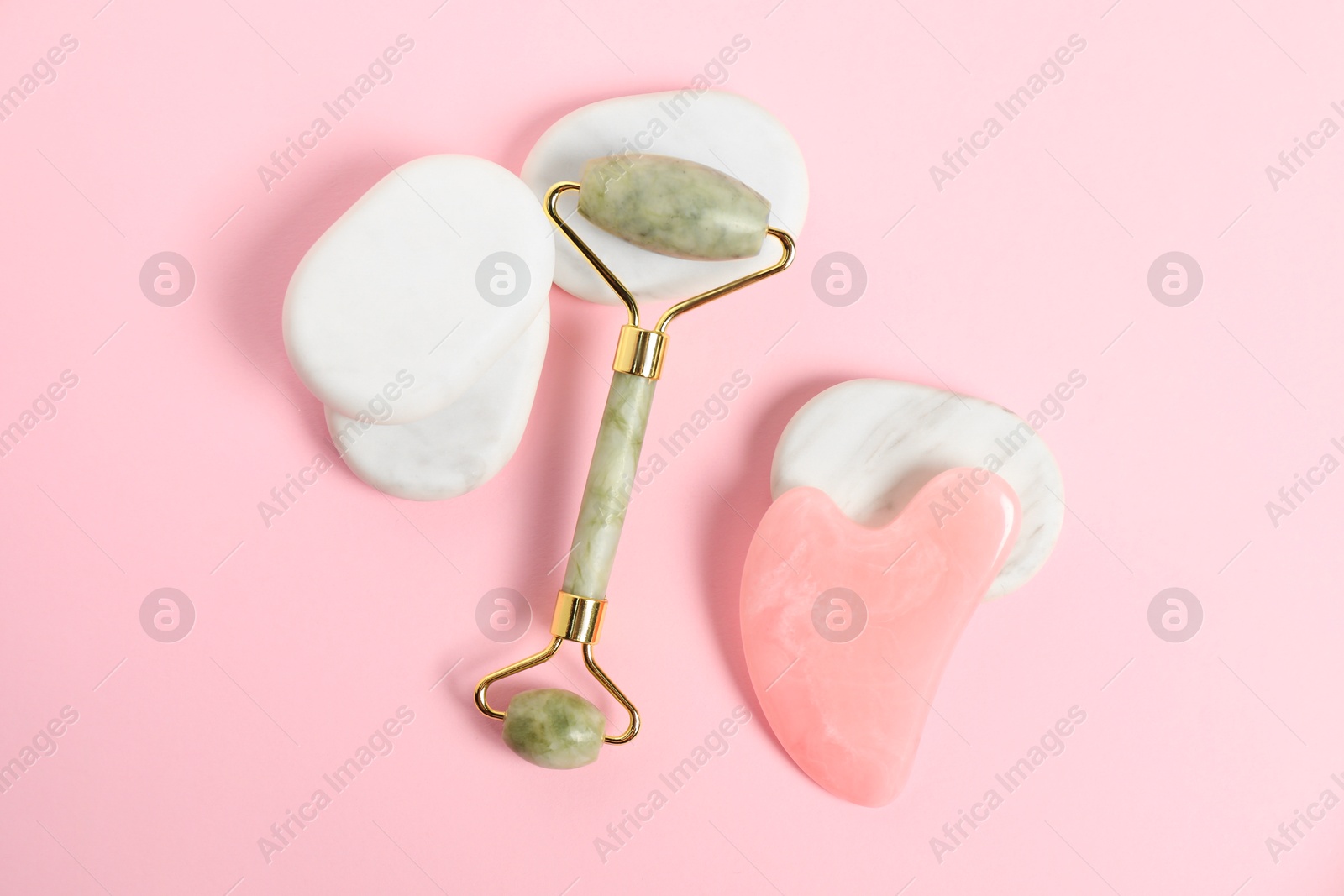 Photo of Face roller, gua sha tool and massage stones on pink background, top view