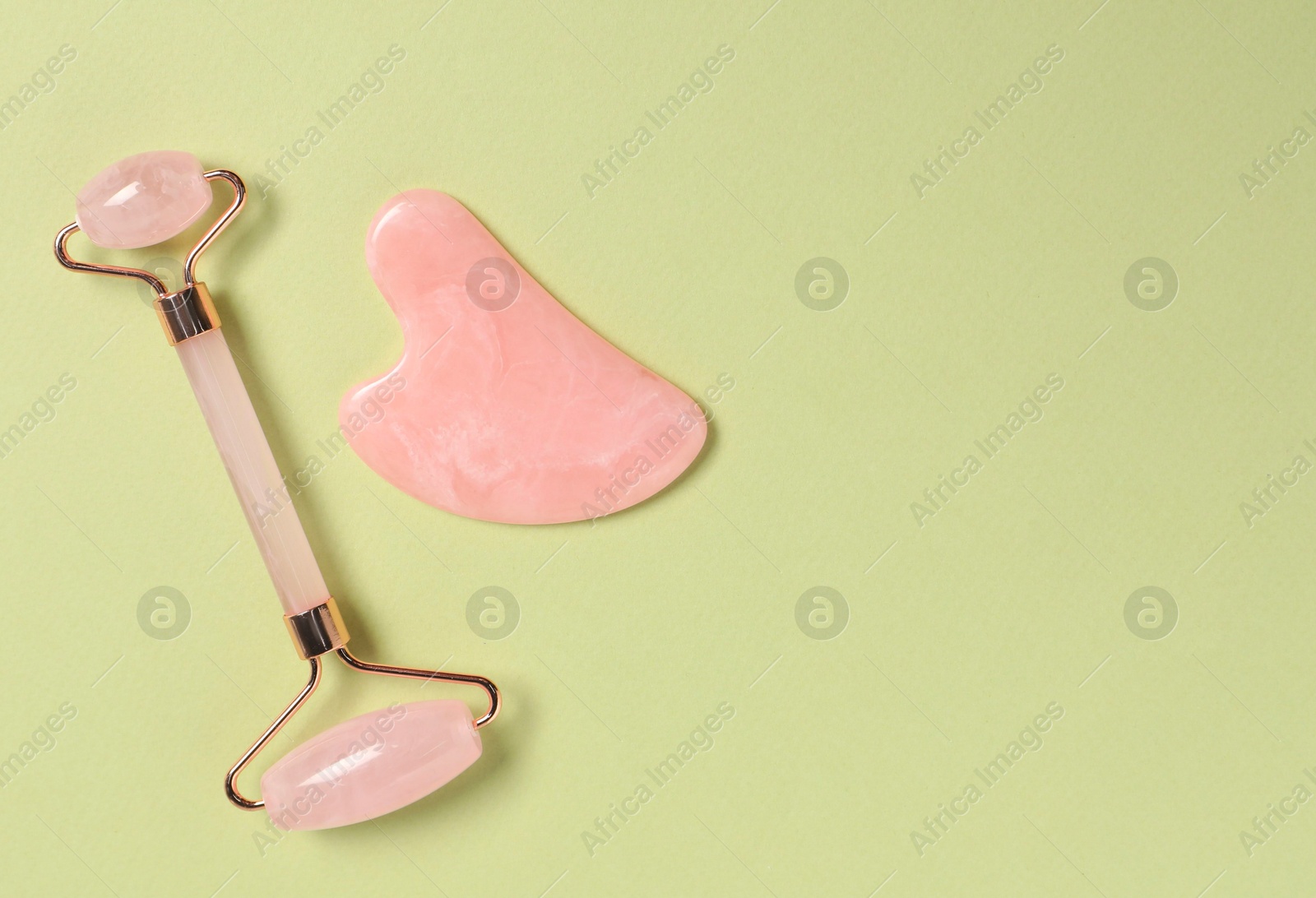 Photo of Face roller and gua sha tool on light green background, top view. Space for text