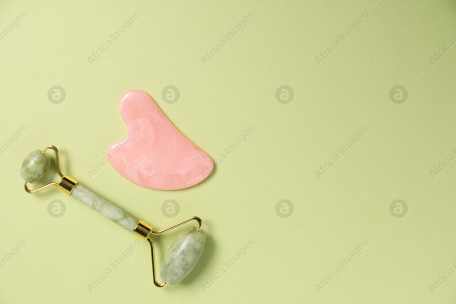 Photo of Face roller and gua sha tool on light green background, top view. Space for text