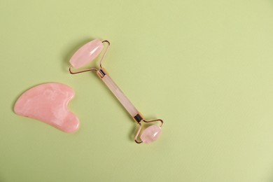 Photo of Face roller and gua sha tool on light green background, top view. Space for text