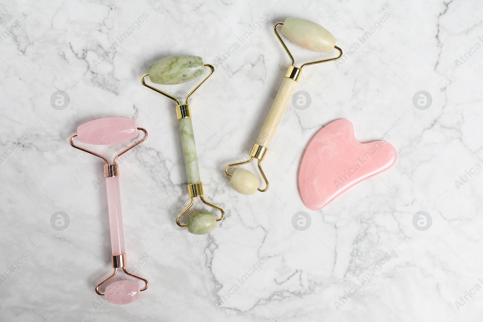 Photo of Face rollers and gua sha tool on white marble background, flat lay