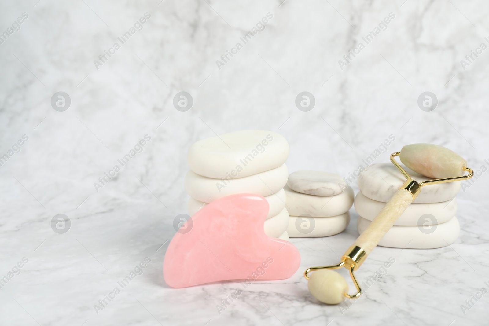 Photo of Face roller, gua sha tool and massage stones on white marble background. Space for text