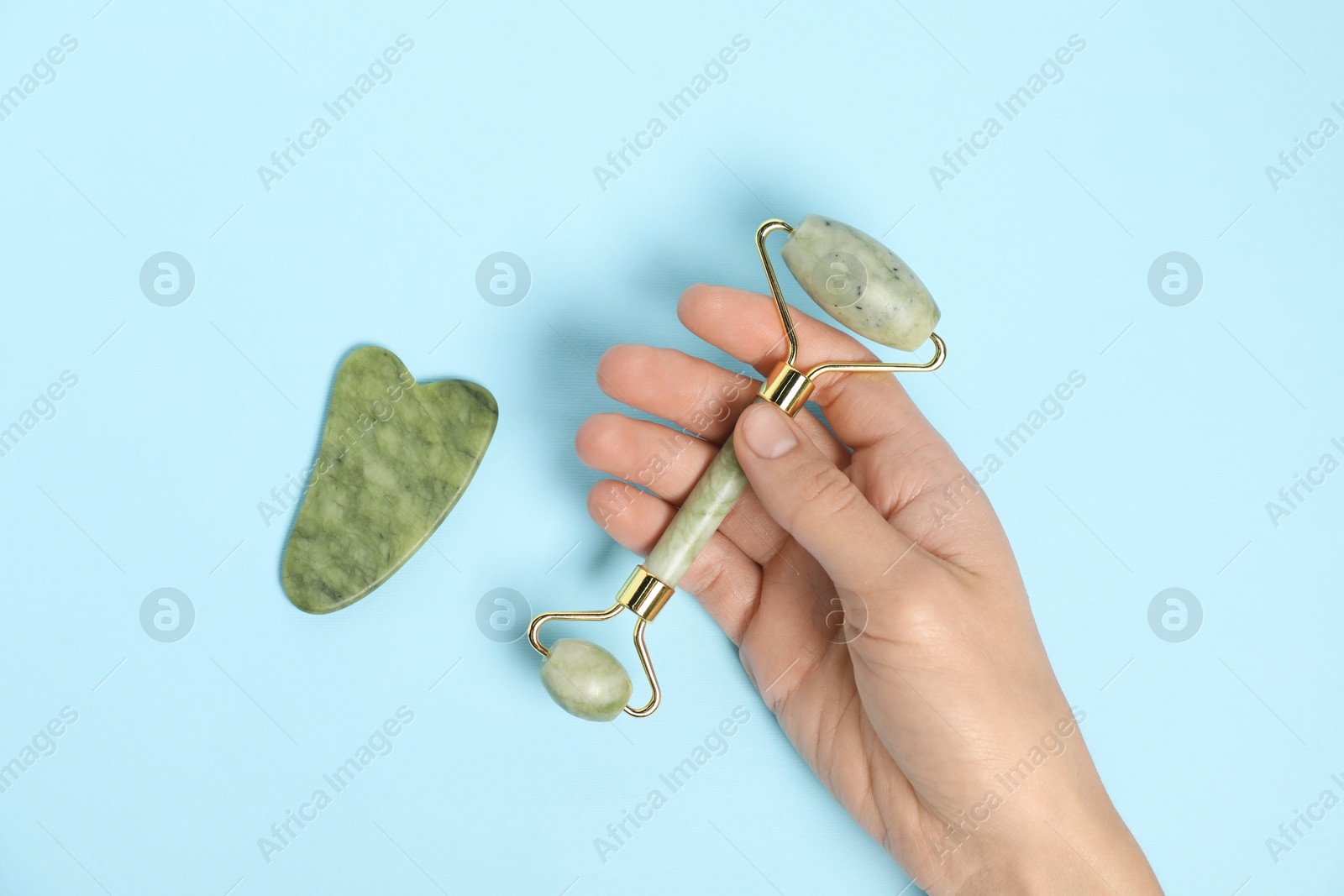 Photo of Woman with face roller and gua sha tool on light blue background, top view