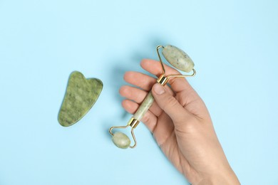 Photo of Woman with face roller and gua sha tool on light blue background, top view