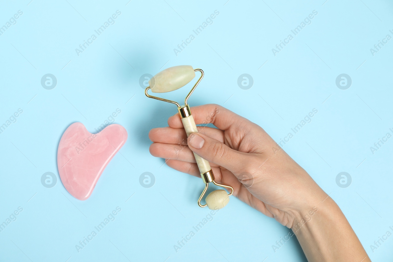 Photo of Woman with face roller and gua sha tool on light blue background, top view