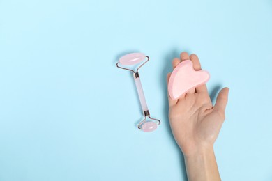 Photo of Woman with face roller and gua sha tool on light blue background, top view. Space for text