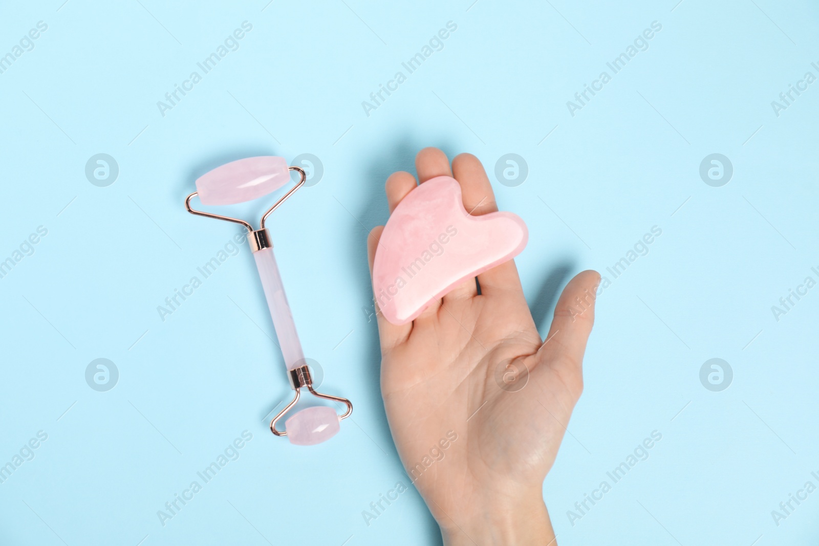 Photo of Woman with face roller and gua sha tool on light blue background, top view