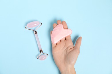 Photo of Woman with face roller and gua sha tool on light blue background, top view