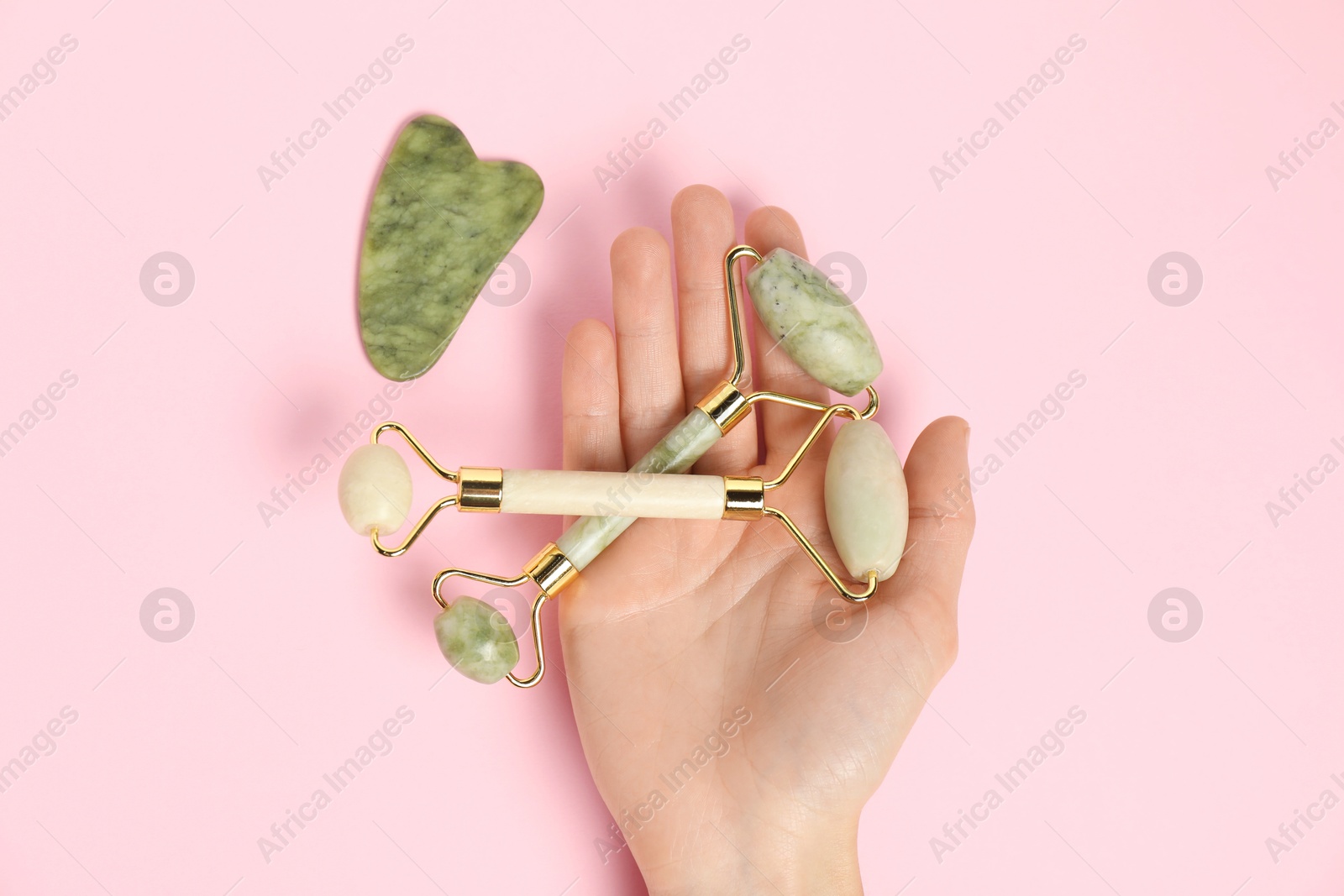 Photo of Woman with face rollers and gua sha tool on pink background, top view