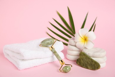 Photo of Face roller, gua sha tool, plumeria flower, massage stones, towel and leaf on pink background