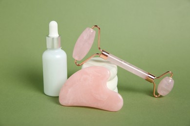 Photo of Face roller, gua sha tool, cosmetic product and massage stones on green background