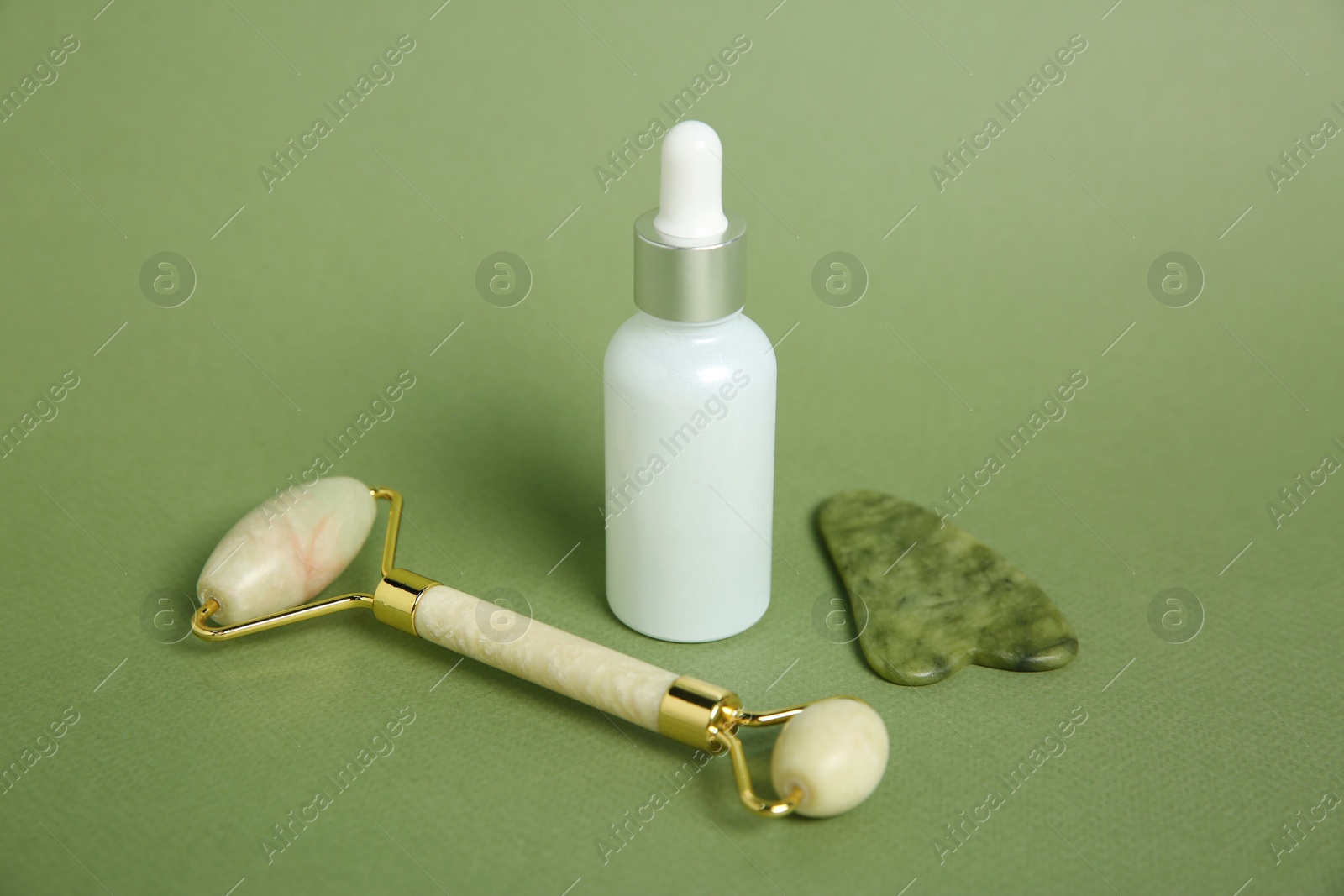 Photo of Face roller, gua sha tool and cosmetic product on green background