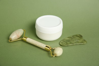 Photo of Face roller, gua sha tool and cosmetic product on green background