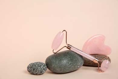 Photo of Face roller, gua sha tool and stones on beige background. Space for text