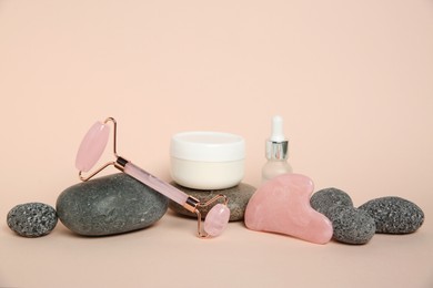 Photo of Face roller, gua sha tool, cosmetic products and stones on beige background