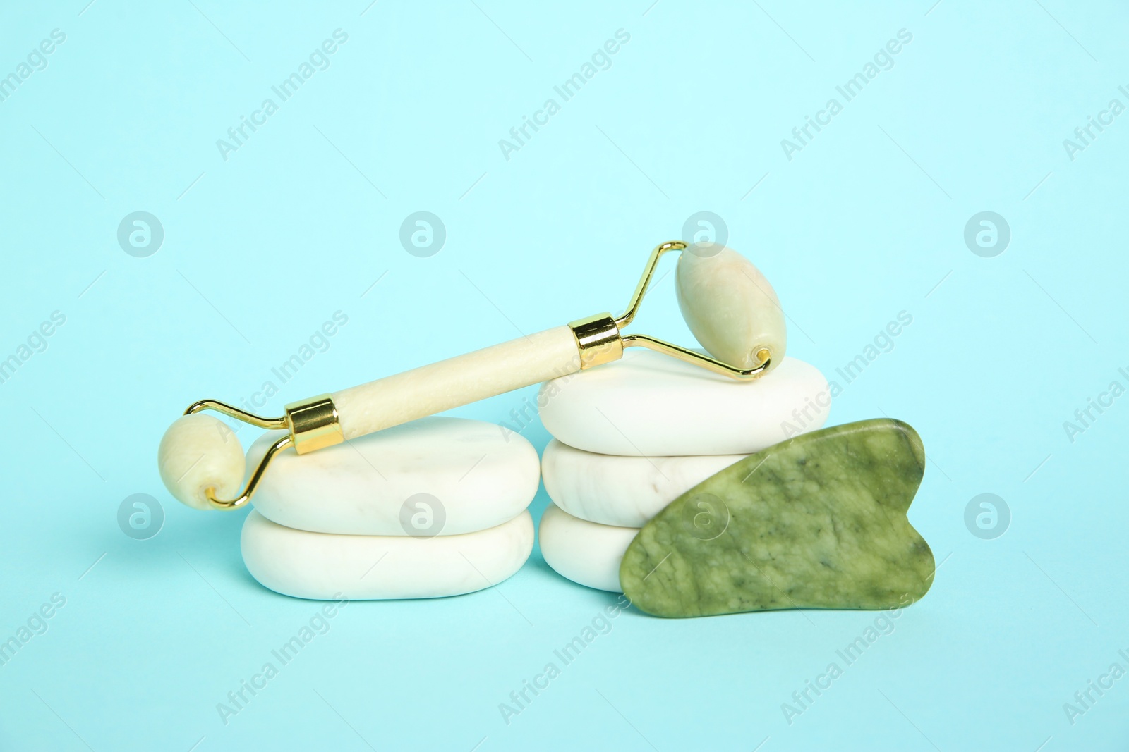 Photo of Face roller, gua sha tool and massage stones on light blue background