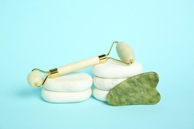 Photo of Face roller, gua sha tool and massage stones on light blue background