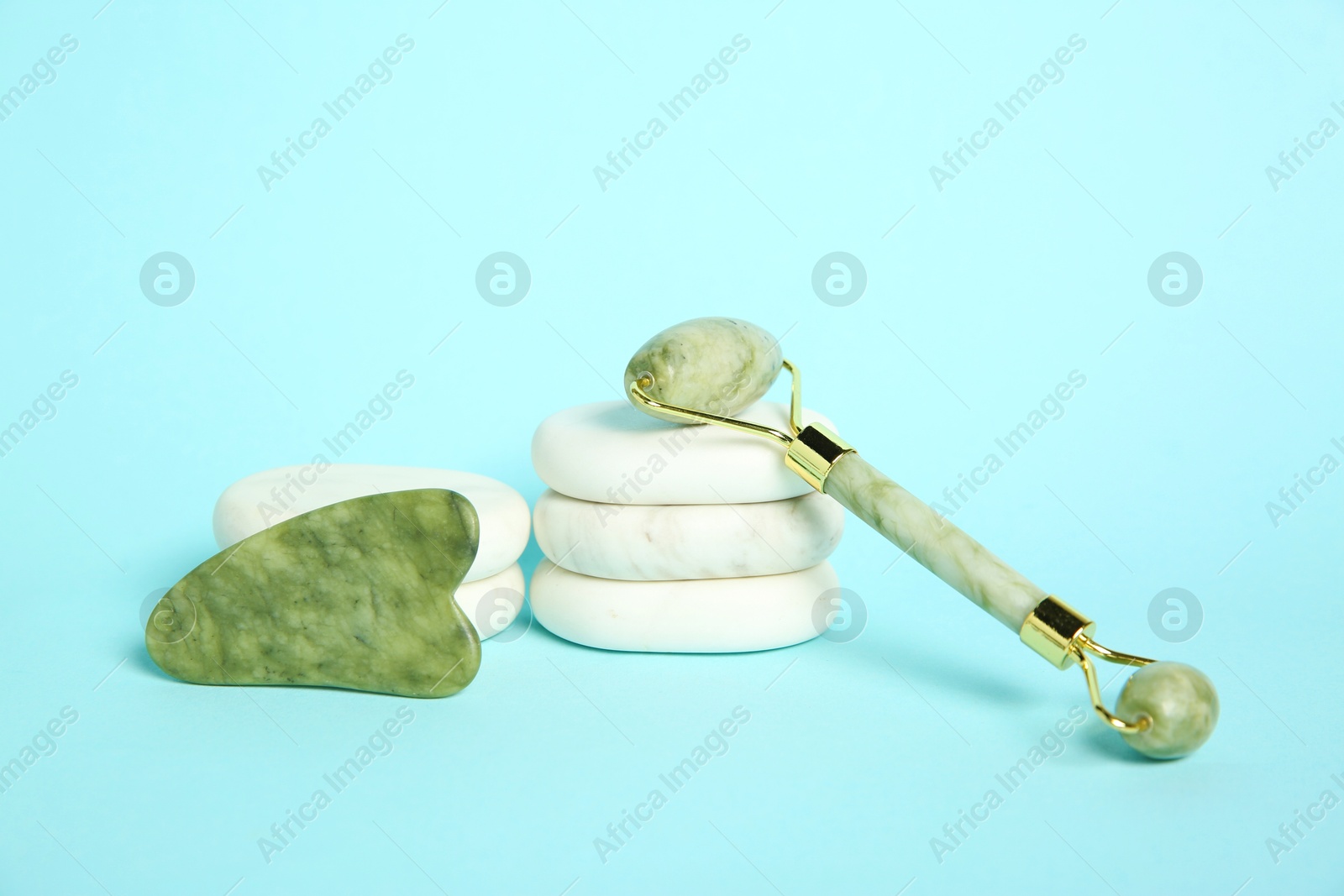 Photo of Face roller, gua sha tool and massage stones on light blue background