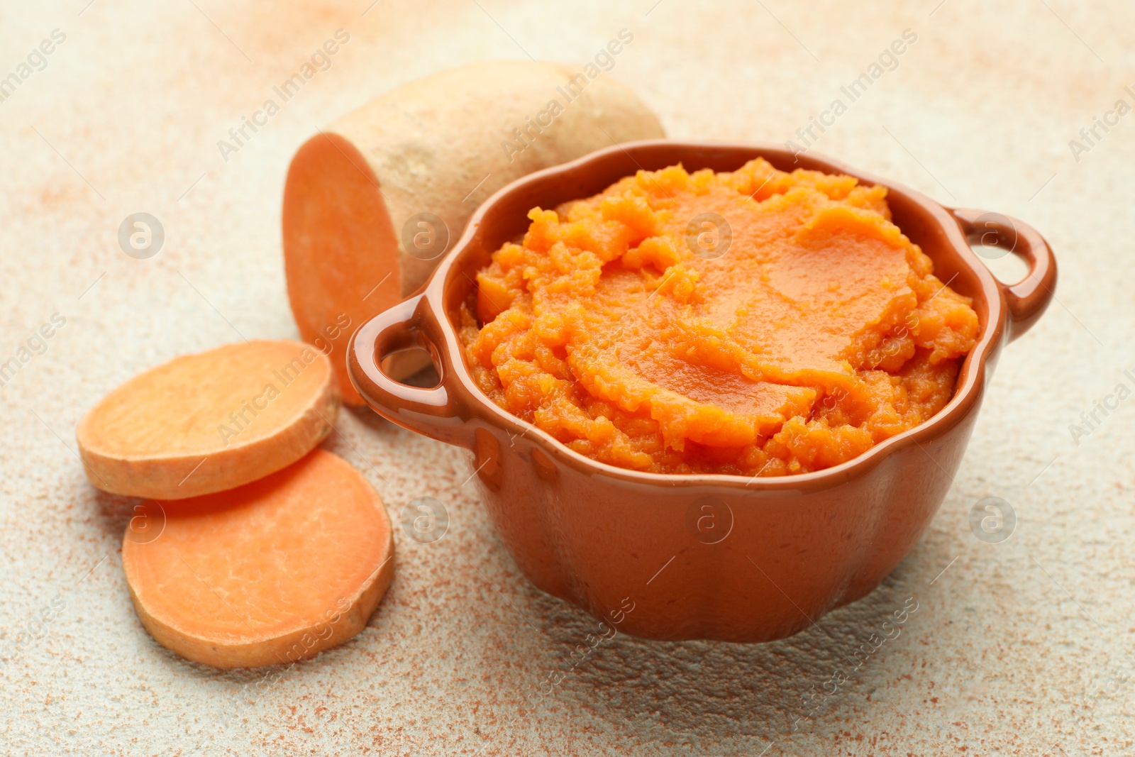 Tasty mashed sweet potato in bowl and cut vegetable on beige textured table, closeup Photo of Tasty mashed sweet potato in bowl and cut vegetable on beige textured table, closeup