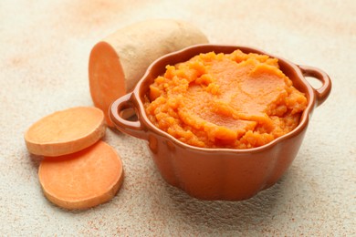 Photo of Tasty mashed sweet potato in bowl and cut vegetable on beige textured table, closeup