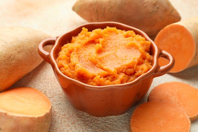 Photo of Tasty mashed sweet potato in bowl and fresh vegetables on beige textured table, closeup