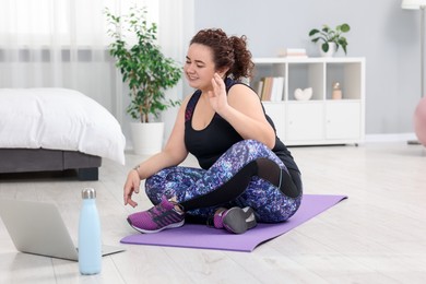 Photo of Plus size woman having fitness training with online coach via laptop at home