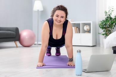 Photo of Plus size woman having fitness training with online coach via laptop at home