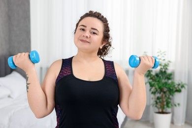 Photo of Plus size woman with dumbbells training at home