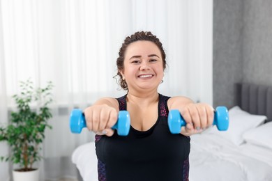 Photo of Plus size woman with dumbbells training at home