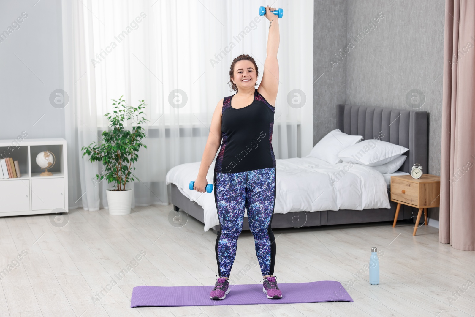 Photo of Plus size woman with dumbbells training at home