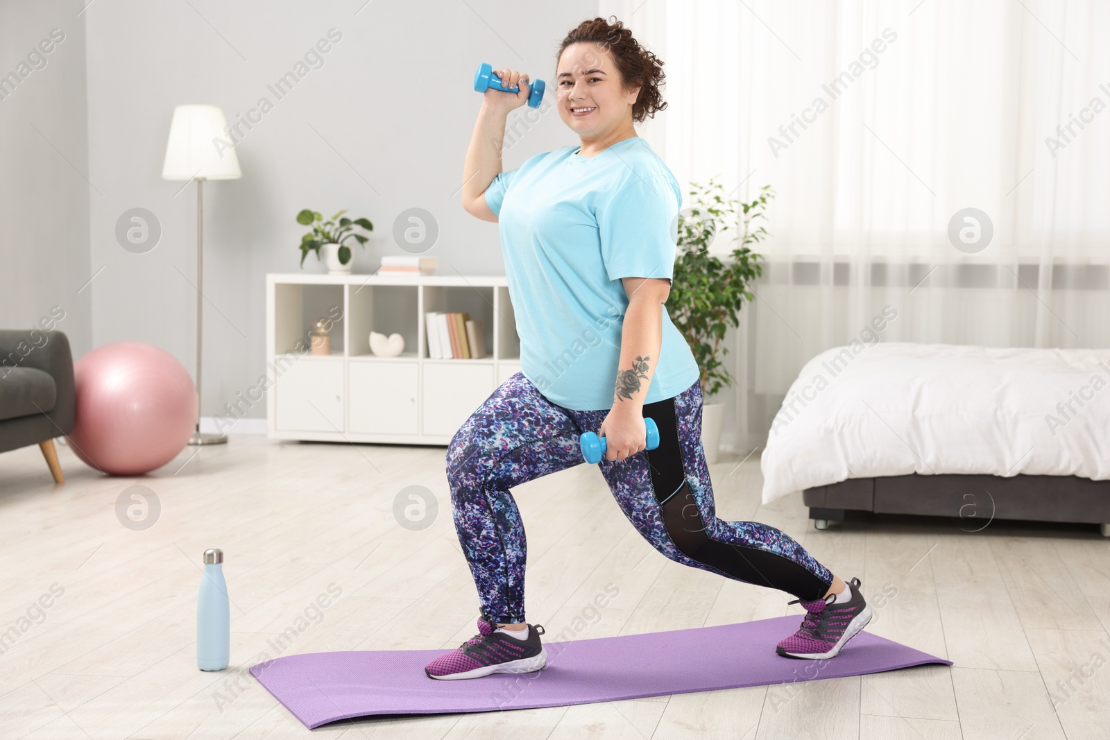 Photo of Plus size woman with dumbbells training at home