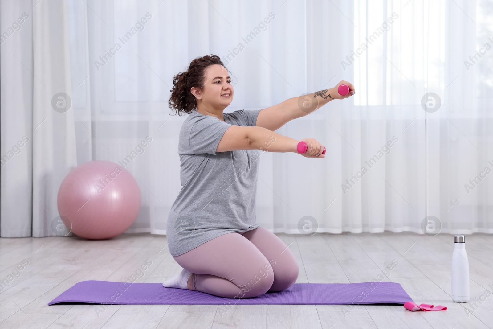 Photo of Plus size woman with dumbbells training at home