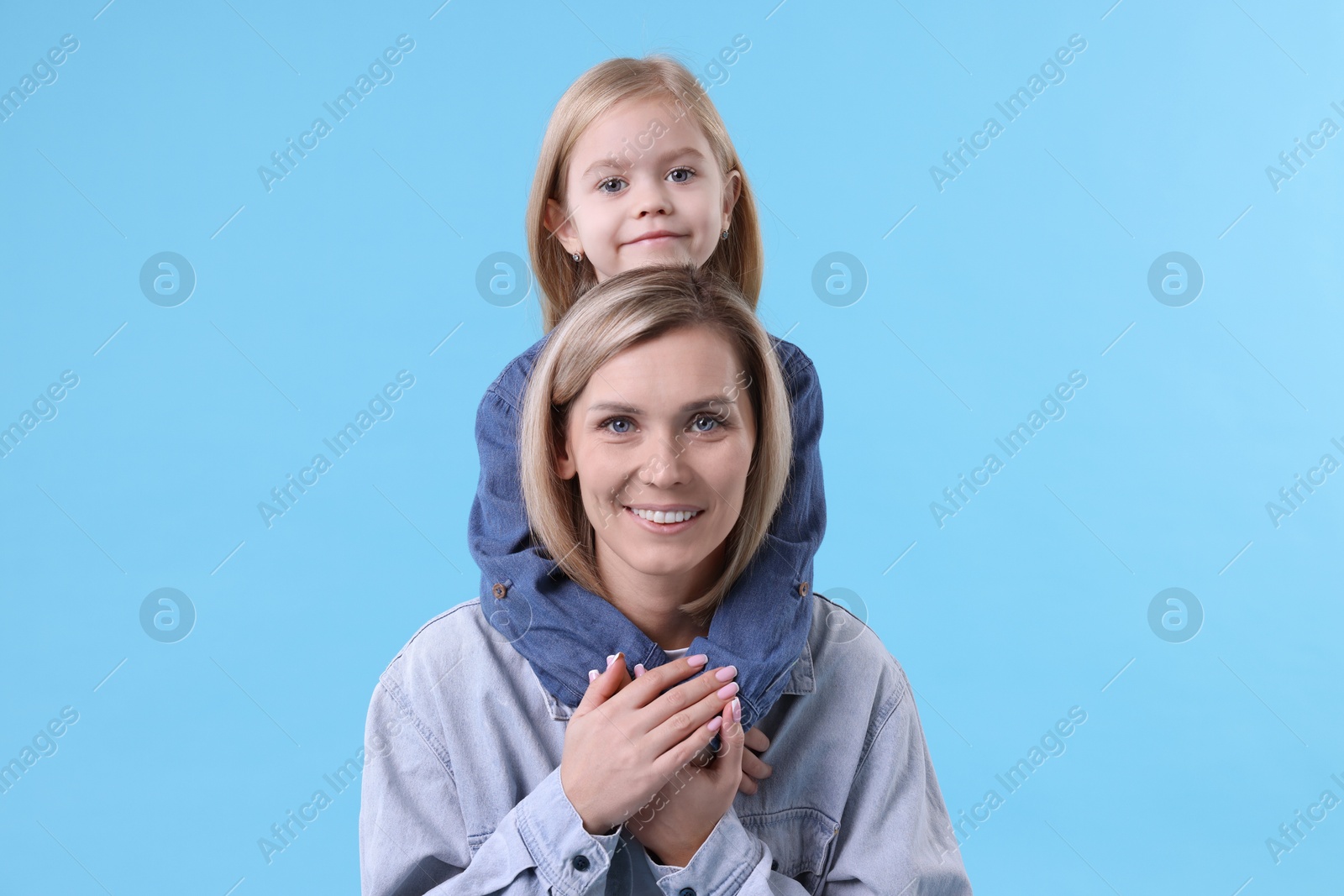 Photo of Cute little girl hugging her mom on light blue background. Happy Mother's Day