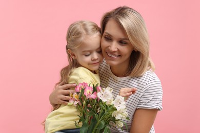 Photo of Little daughter congratulating her mom with bouquet of alstroemeria flowers on pink background. Happy Mother's Day