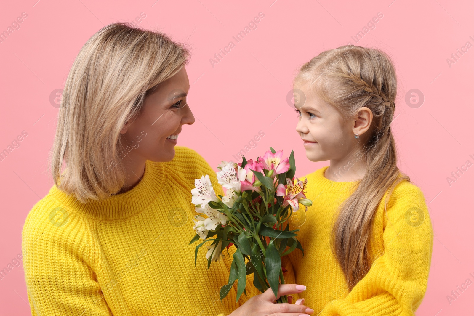 Photo of Little daughter congratulating her mom with bouquet of alstroemeria flowers on pink background. Happy Mother's Day