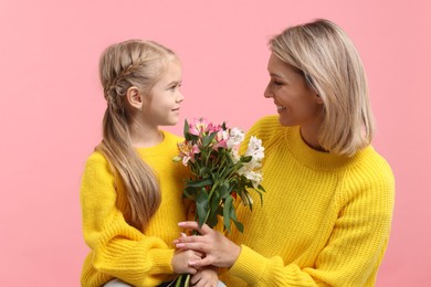 Little daughter congratulating her mom with bouquet of alstroemeria flowers on pink background. Happy Mother's Day